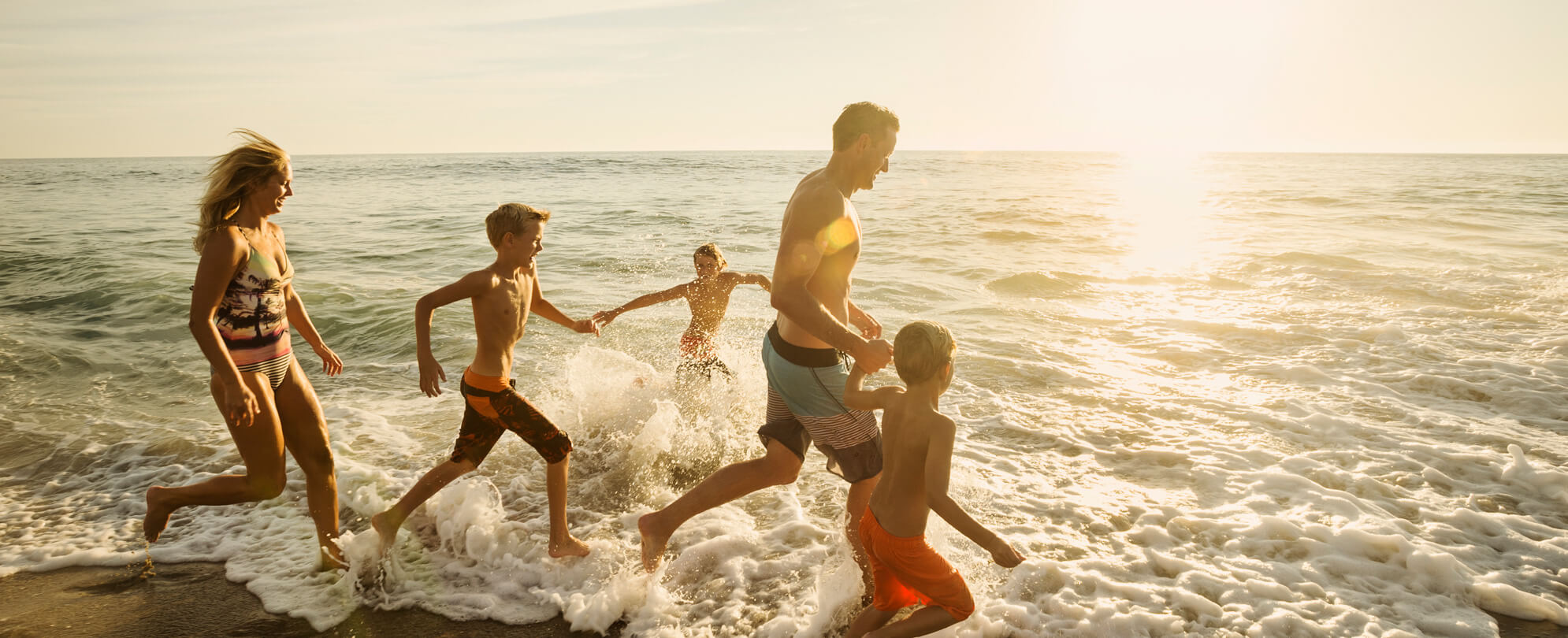 Father, mother, and their three young sons running into the ocean at sunset