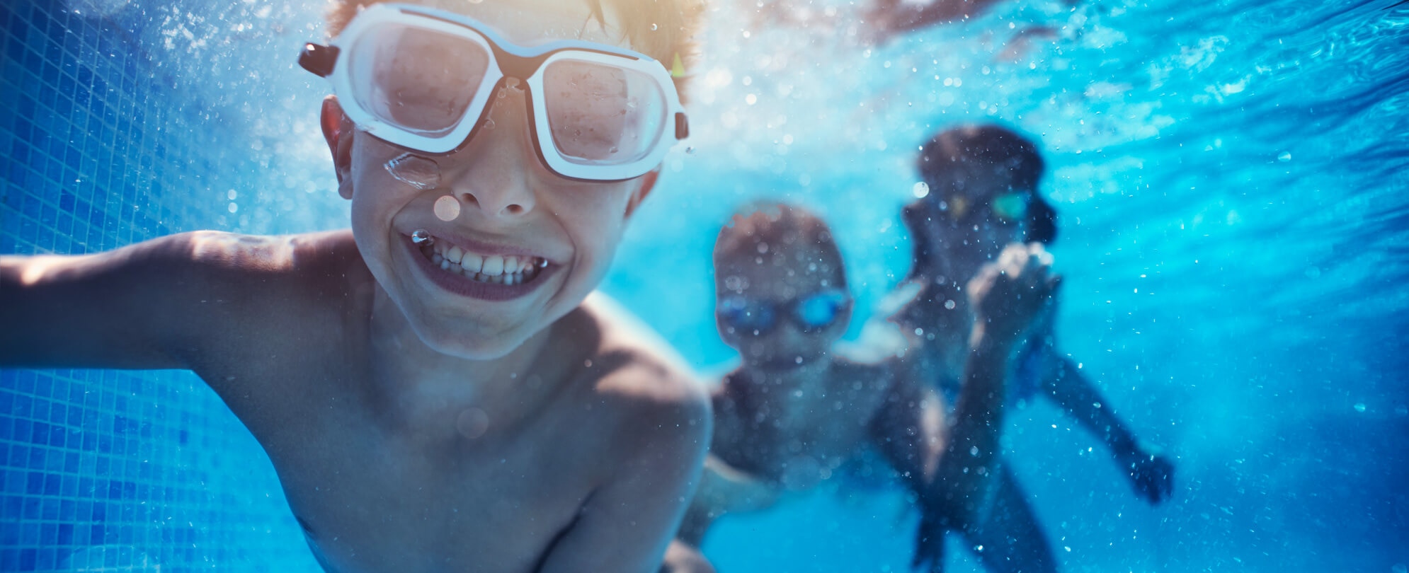 young boy wearing goggles smiling underwater 