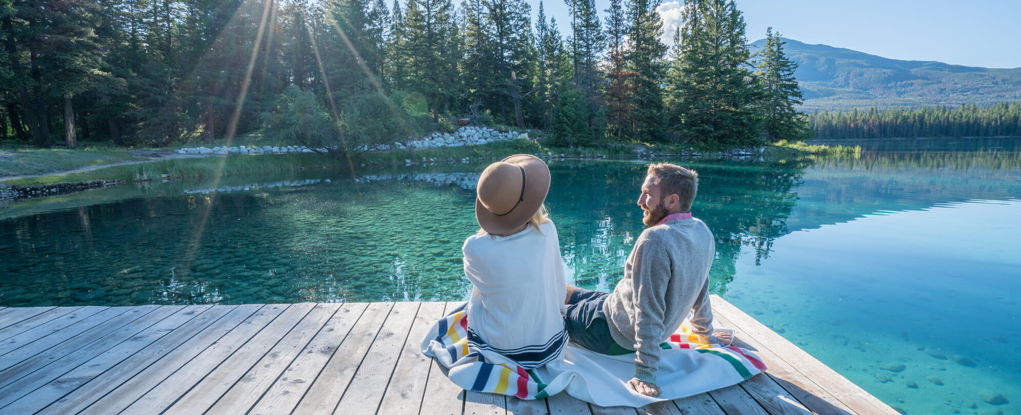 Couple sitting together on a dock overlooking lush trees and crystal clear waters 