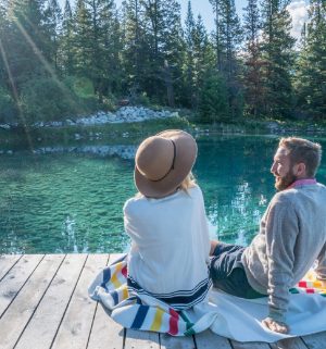 Couple sitting together on a dock overlooking lush trees and crystal clear waters 