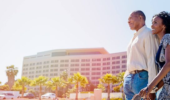 Couple holding each other in front of a resort and looking into the distance 