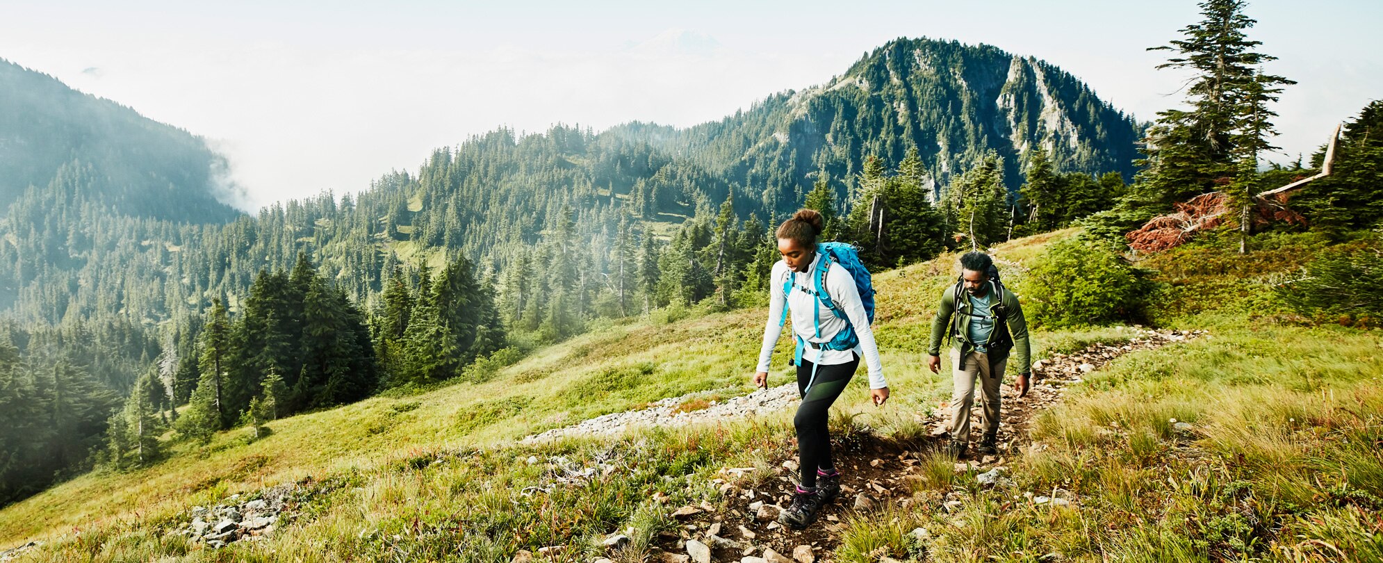 Father and daughter hiking up a lush mountainside 