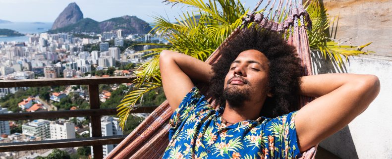 Man laying with his eyes shut in a hammock surrounded by palm trees 