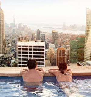 Couple leaning on the edge of an infinity pool overlooking city views 