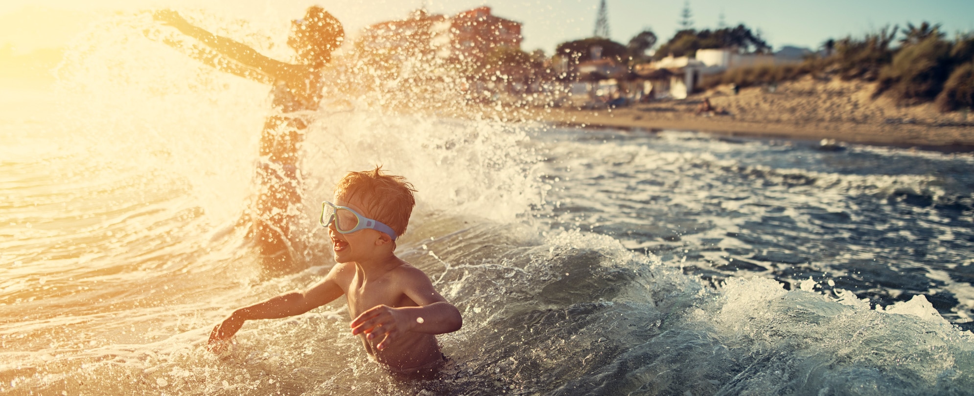 Little boy wearing goggle crashing into an ocean wave 