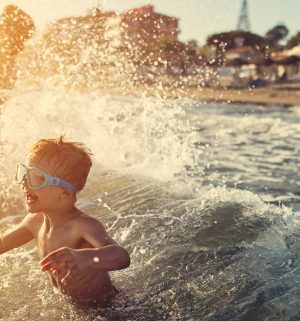 Little boy wearing goggle crashing into an ocean wave 