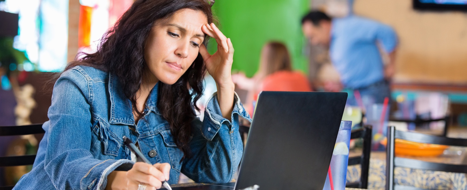 Worried young businesswoman checking finances on computer in restaurant