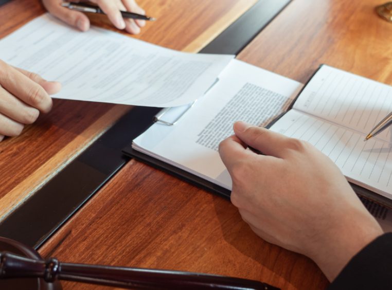 Cropped Hands Of Judge Writing In Book With Businessman At Desk