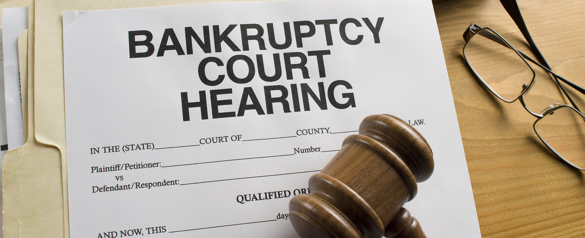 Partial view of a gavel atop a bankruptcy court hearing document with a pair of glasses resting on a desk