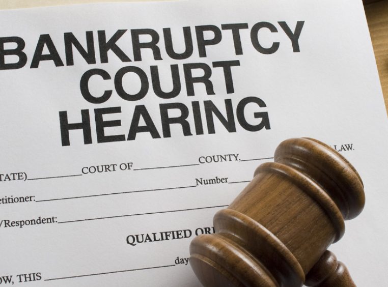 Partial view of a gavel atop a bankruptcy court hearing document with a pair of glasses resting on a desk