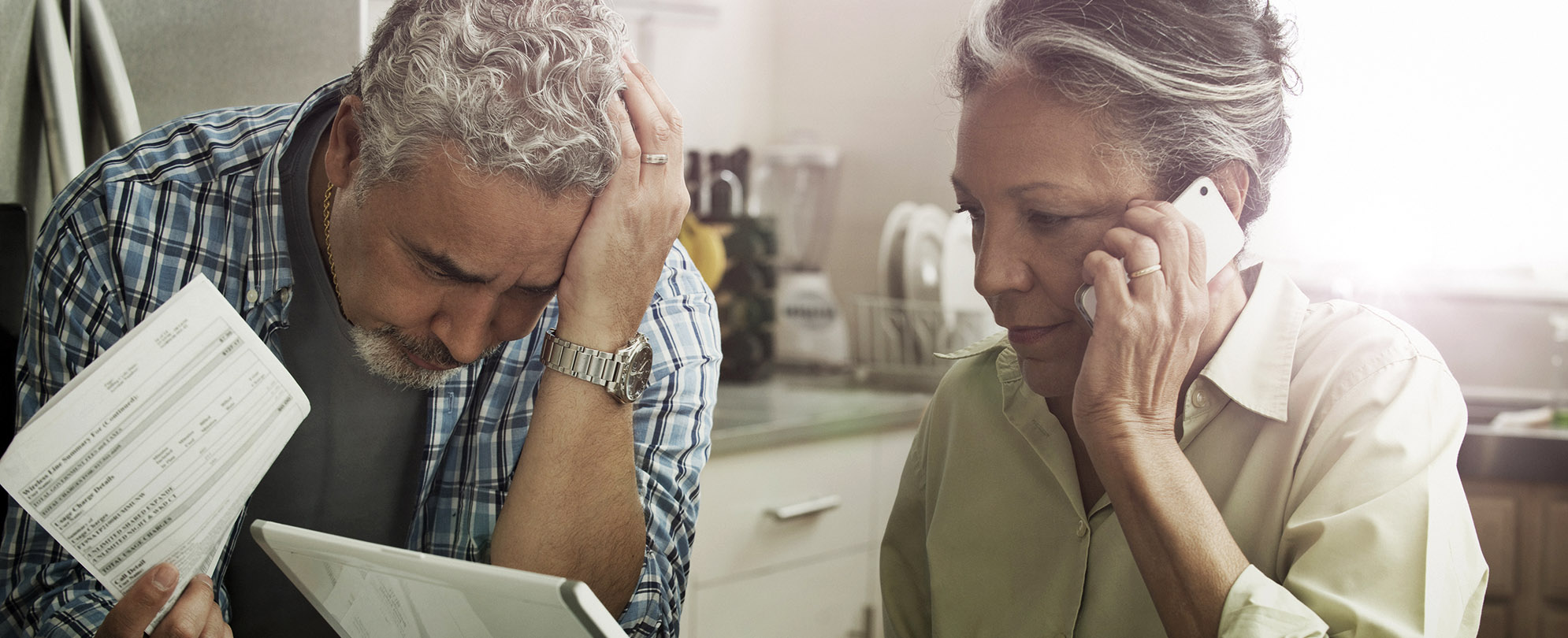 Stressed couple paying bills, woman on laptop and phone while man looks through papers