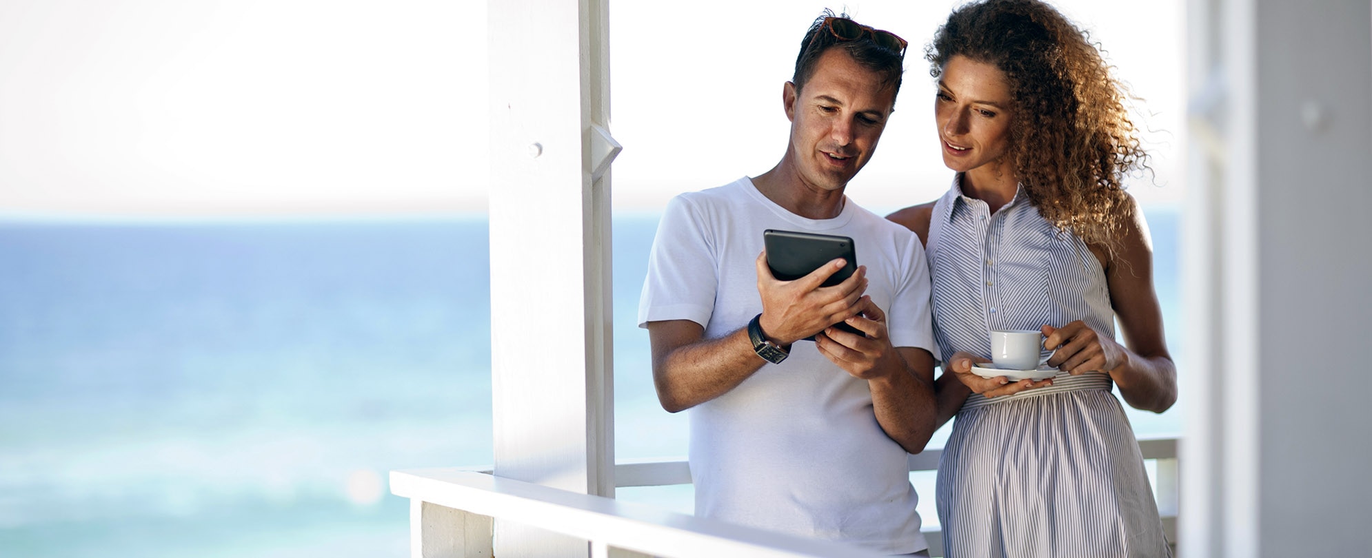 Couple having their morning coffee on a balcony overlooking the ocean while reviewing documents on an iPad 