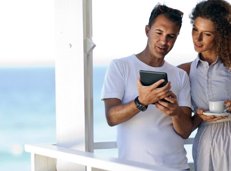 Couple having their morning coffee on a balcony overlooking the ocean while reviewing documents on an iPad 
