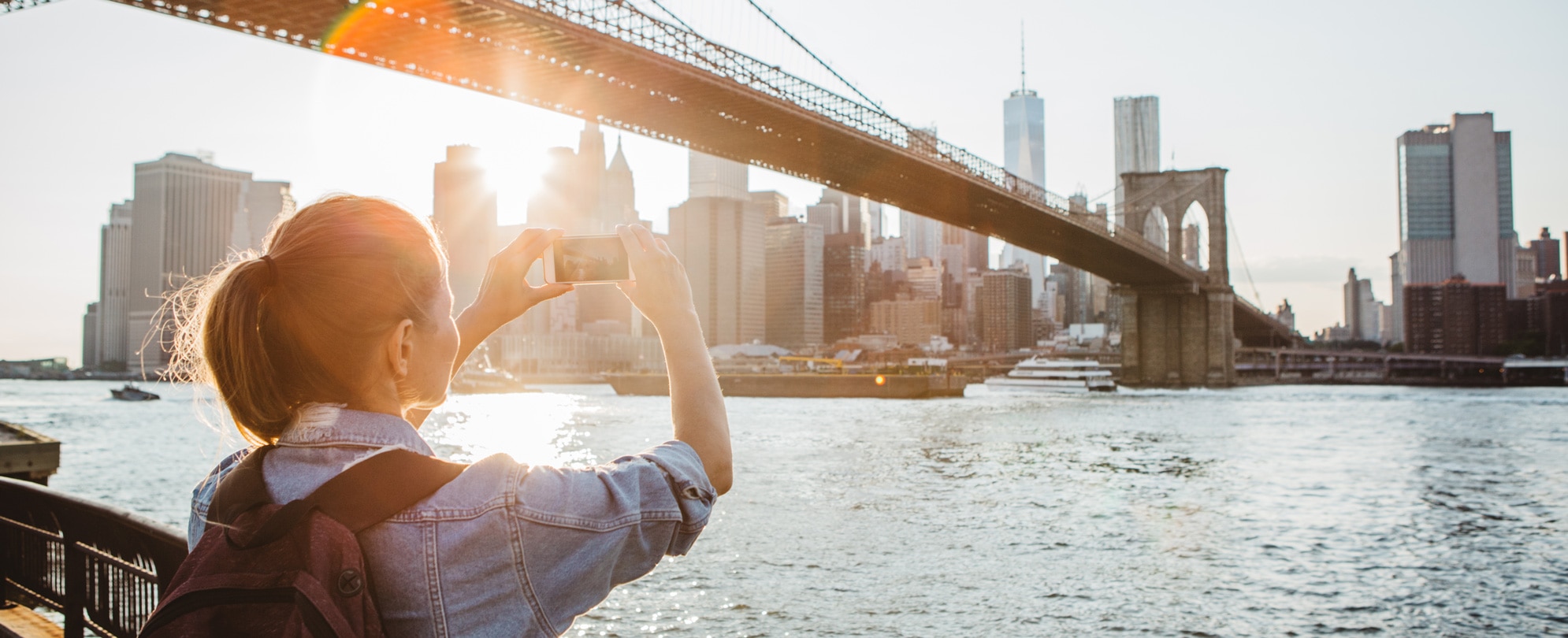 Woman taking a photograph with her phone of the Brooklyn Bridge in New York, NY. 