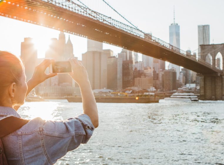 Woman taking a photograph with her phone of the Brooklyn Bridge in New York, NY. 