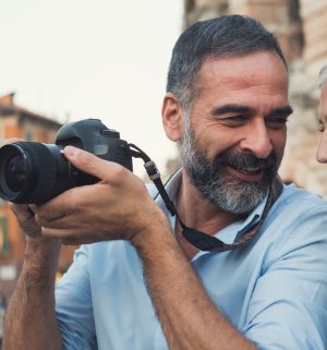 Man smiling in baby blue shirt holding up his DSLR camera 