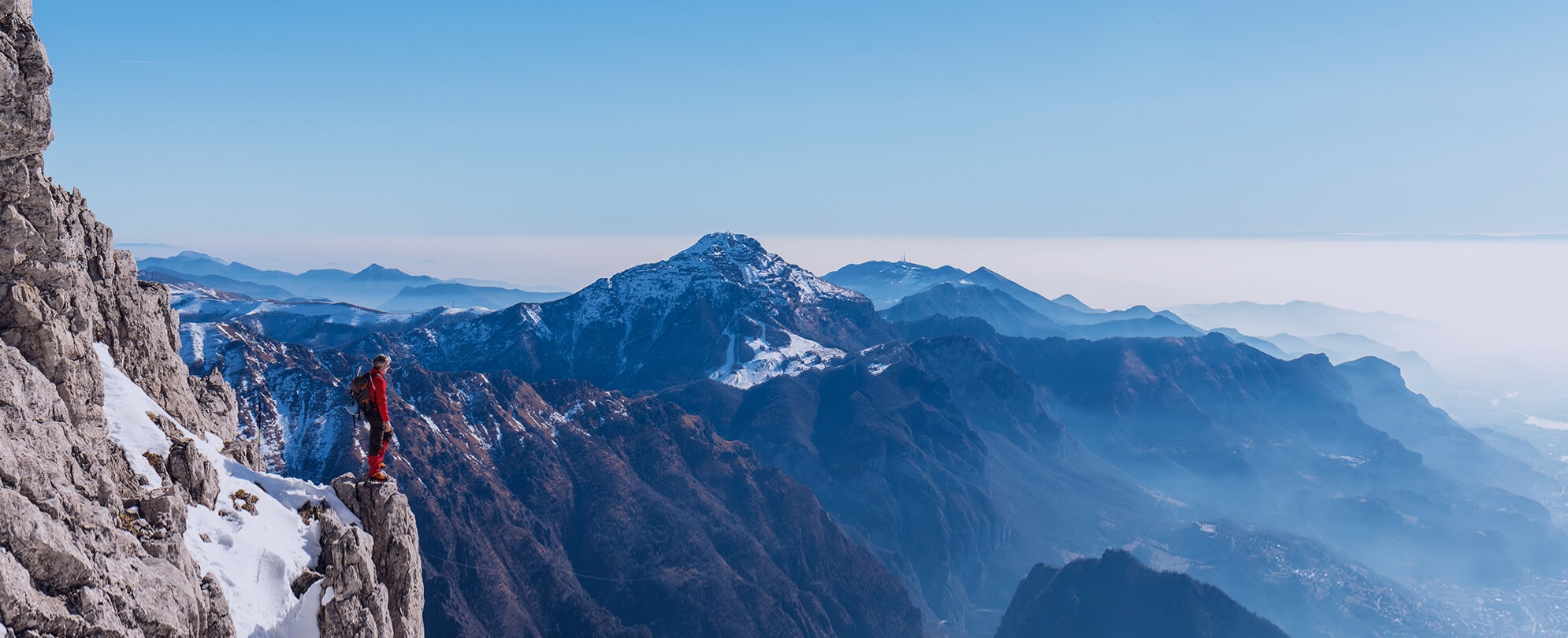 Mountaineer in red racket overlooking lush snow-covered mountains